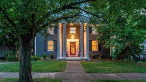 A two-story house with a front porch, columns, and a red door.