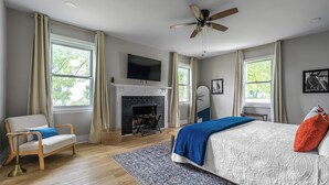 A bedroom with a bed, a chair, a fireplace, and a ceiling fan.