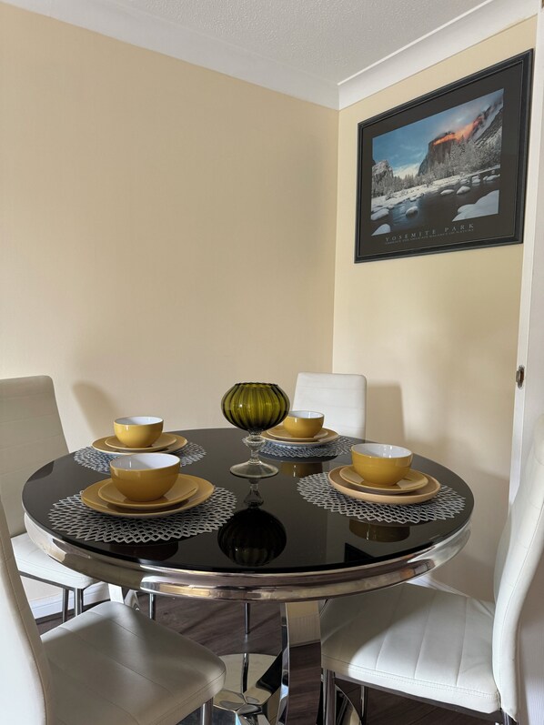 A dining table with yellow bowls and a green glass centerpiece, surrounded by white chairs. - Cosy HLA king court 3  (Motherwell)