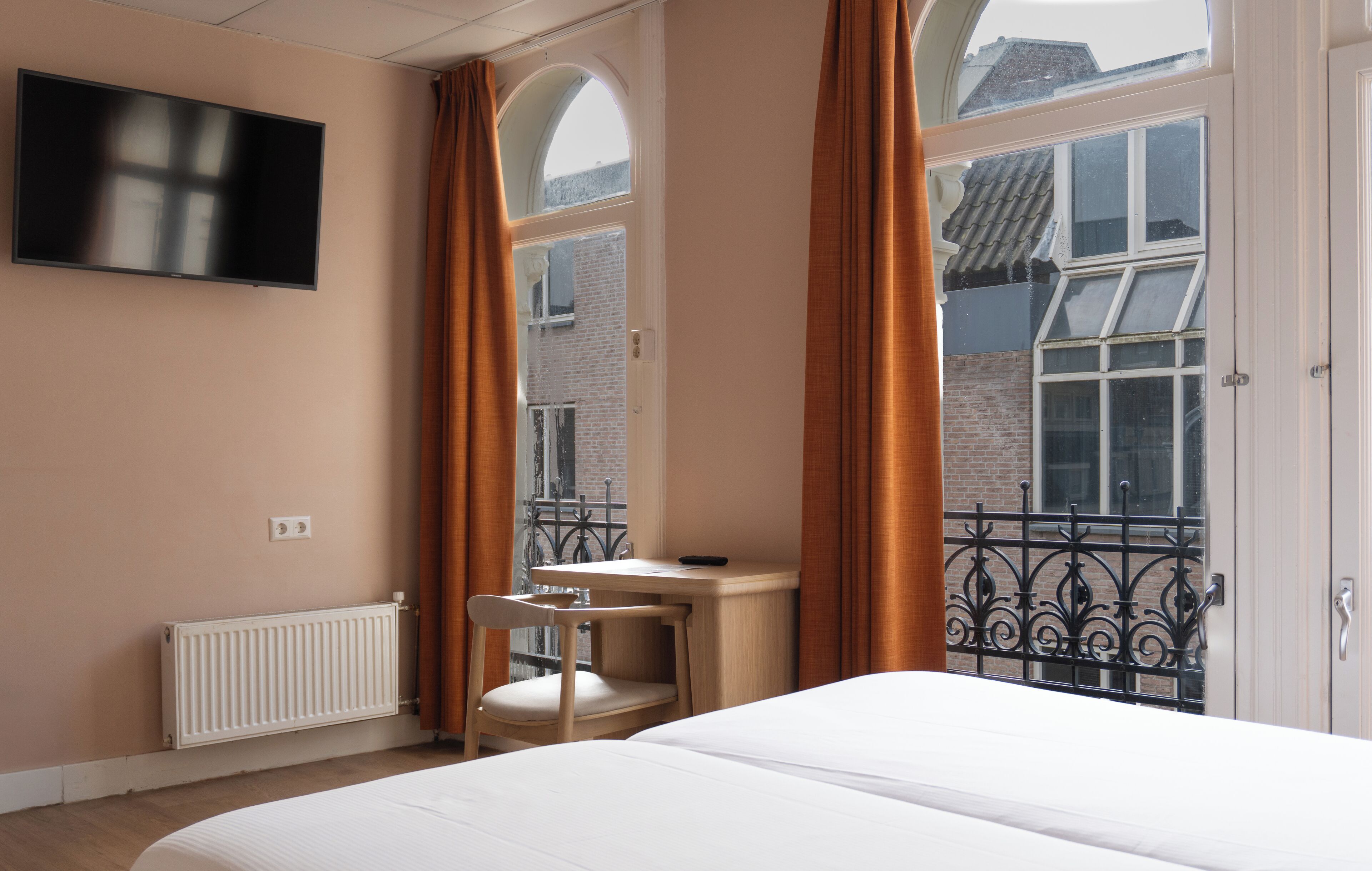 A hotel room with a bed, a desk, a chair, a TV, and a window with curtains.