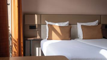 Une chambre d’hôtel avec un lit, deux oreillers, une table de chevet et une fenêtre avec des rideaux.