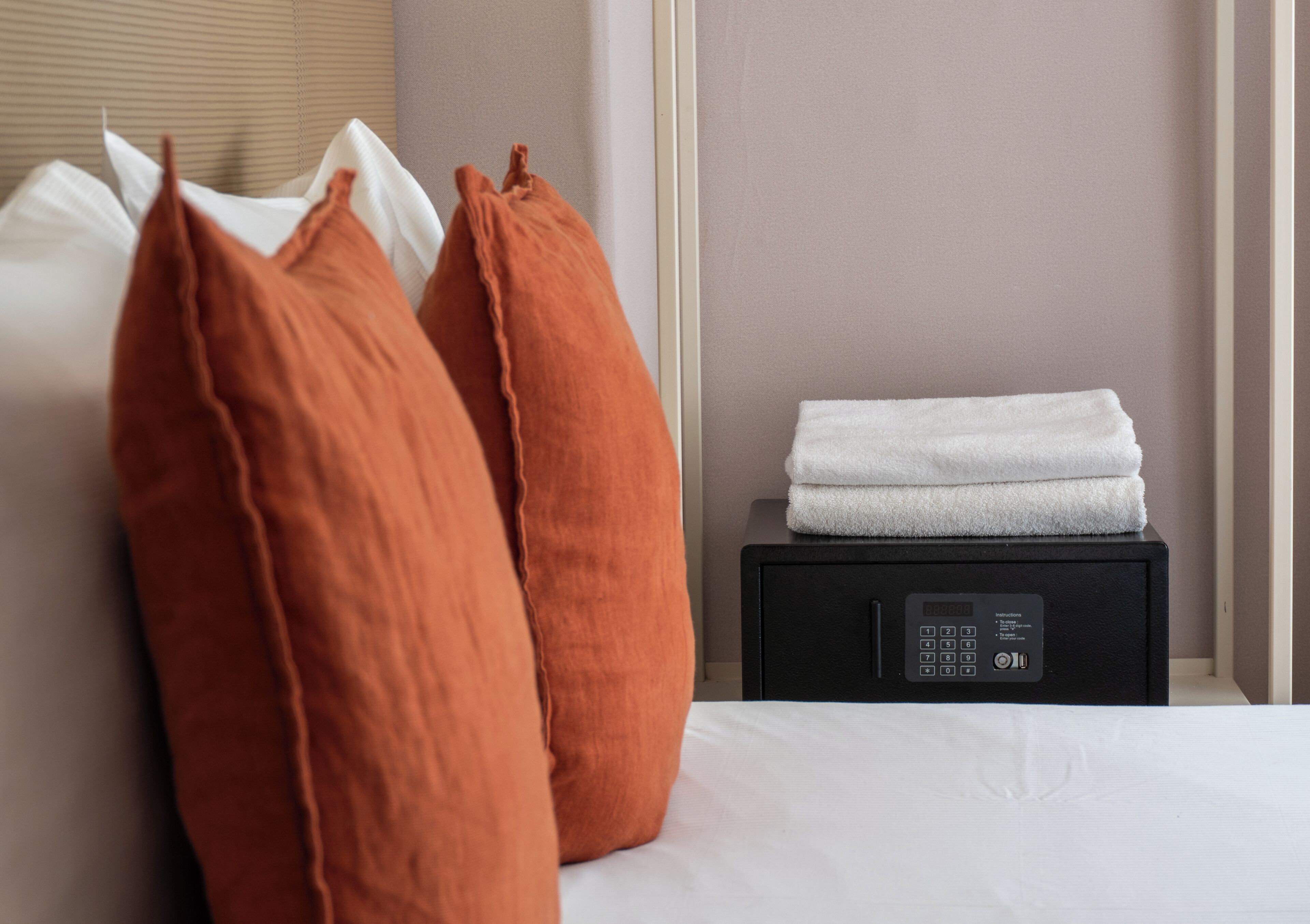 A neatly made bed with white linens, a black bedside table with a remote control, and two orange pillows.