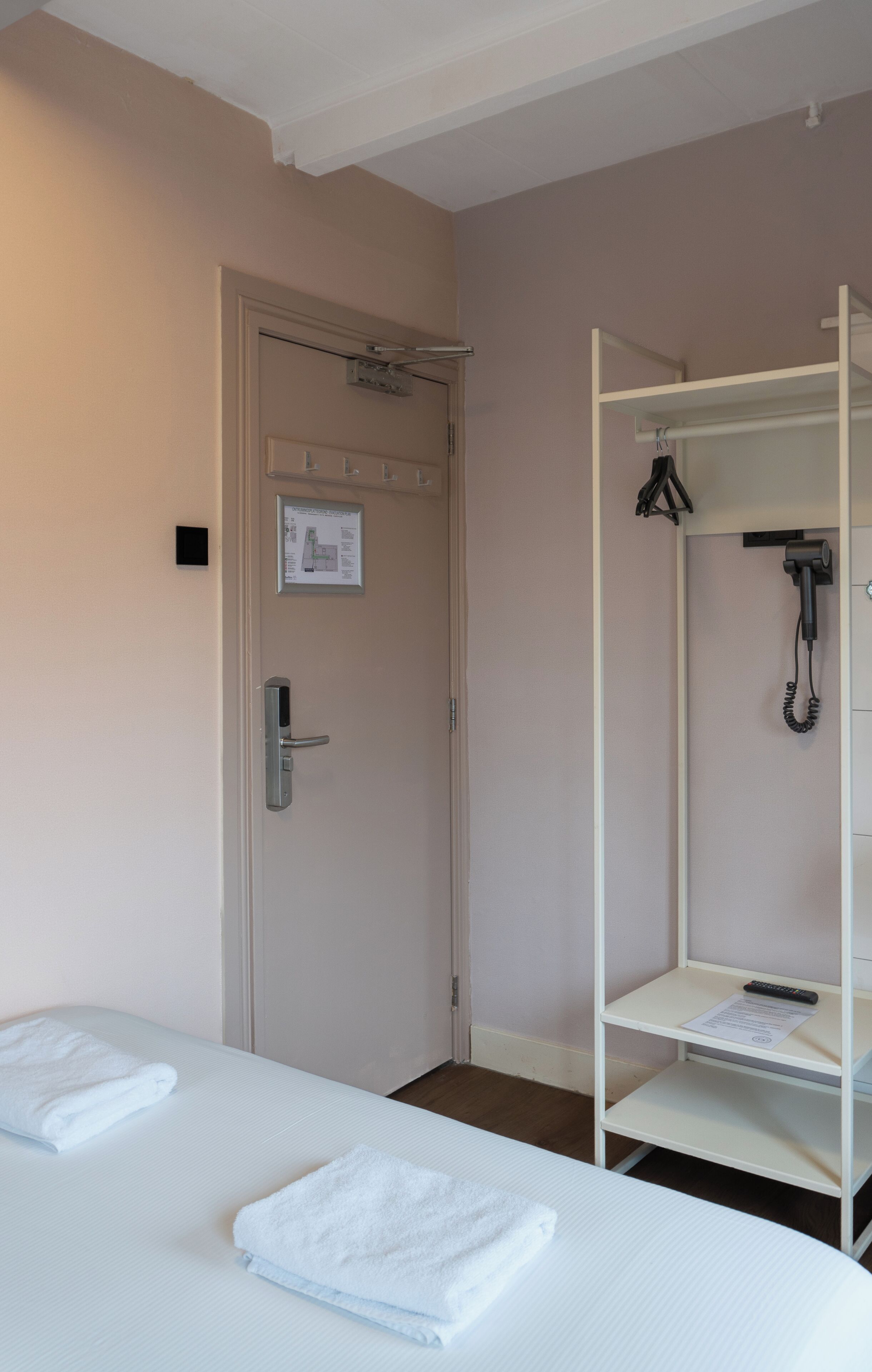 Una habitación de hotel con cama, puerta con cerradura, zona de ducha con toallero y estante con toalla.