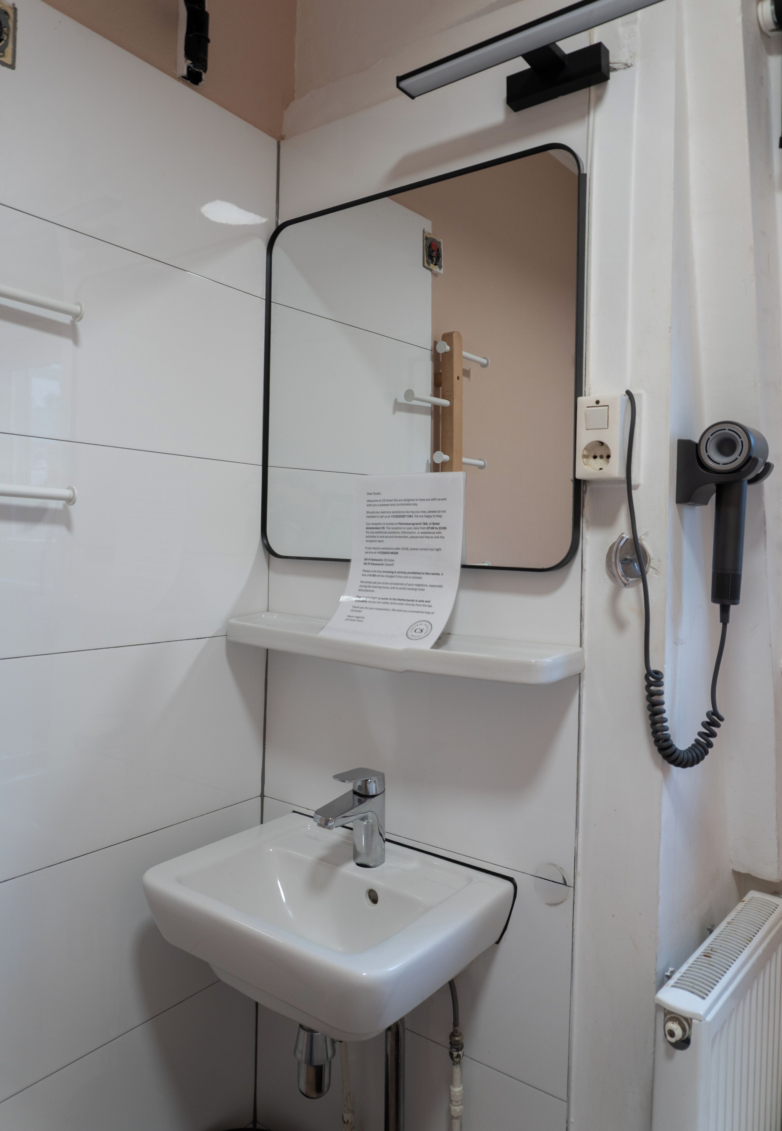 Een badkamer met een witte wastafel, een spiegel en een haardroger aan de muur.