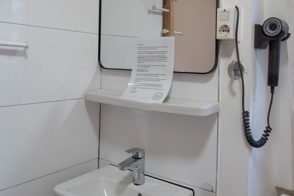 A bathroom with a white sink, a mirror, and a hairdryer on a wall.