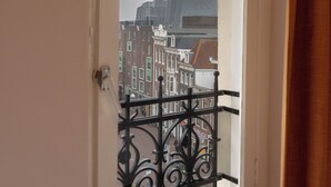 A view through a window with a black wrought iron balcony railing, a white door frame, and a glimpse of buildings in the background. - CS Hotel (Amsterdam)