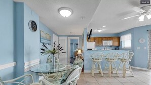 A dining area with a glass table and wicker chairs, a kitchen with white cabinets and a microwave, and a ceiling fan. - Flipflops & fun! Charming 2-bedroom ocean view condo at Myrtle Beach Resort (Myrtle Beach)
