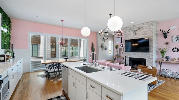 Une cuisine moderne dotée d’un grand îlot central, de meubles blancs et d’un mur d’accent rose.