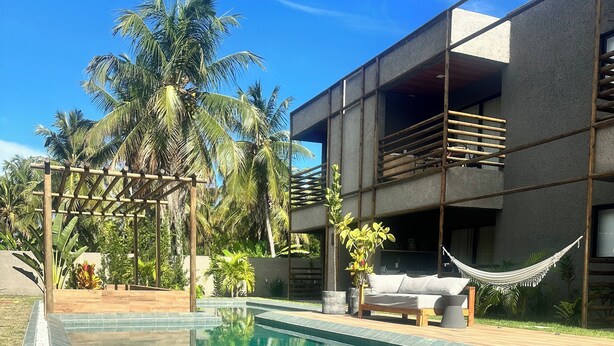 Ein Swimmingpool mit klarem Wasser, umgeben von einer Holzterrasse und einem modernen Gebäude mit Balkonen.