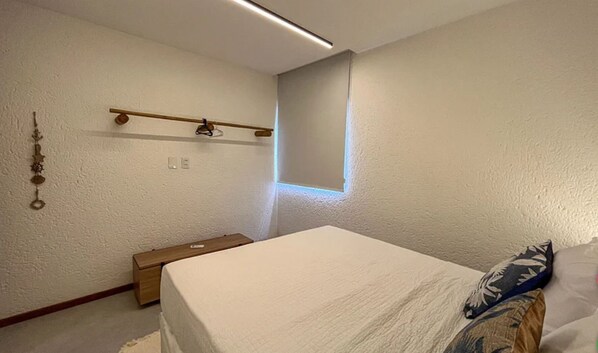 Ein Schlafzimmer mit einem Bett, einem Nachttisch aus Holz, einer Wandablage und einem Fenster mit Jalousien.