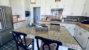 Een moderne keuken met witte kastjes, granieten aanrechtbladen, een roestvrijstalen koelkast, een inbouwoven en een bordje met de tekst 'LAKEHOUSE'.