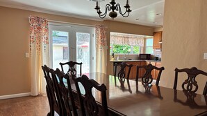 A dining room with a large wooden table and six chairs, a chandelier, and a view of the kitchen through a glass door. - Charming Home in Fairfield, Perfect for Getaways! (Fairfield)