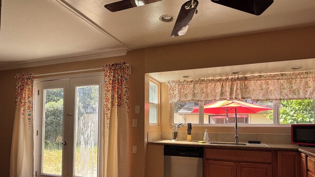 A kitchen with a dishwasher, wooden cabinets, a window with a floral curtain, and a red umbrella outside. - Charming Home in Fairfield, Perfect for Getaways! (Fairfield)