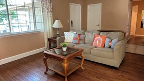 A living room with a beige sofa, a glass coffee table, and a view through a large window. - Charming Home in Fairfield, Perfect for Getaways! (Fairfield)