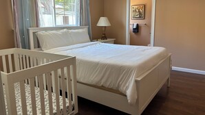 A bedroom with a single bed, a crib, a nightstand, a lamp, and a door with a towel rack. - Charming Home in Fairfield, Perfect for Getaways! (Fairfield)