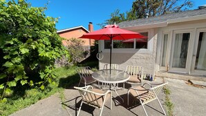 A patio with a round table and four chairs, a red umbrella, and a stone wall. - Charming Home in Fairfield, Perfect for Getaways! (Fairfield)