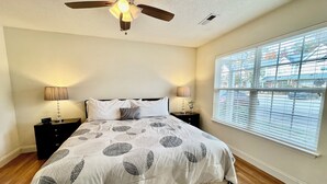 A bedroom with a bed, two bedside tables with lamps, a ceiling fan, and a window with blinds.