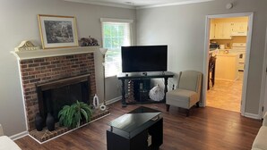 A living room with a fireplace, a flat-screen TV, a coffee table, and a chair.
