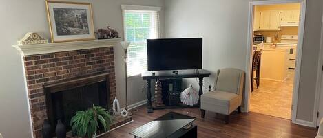 A living room with a fireplace, a flat-screen TV, a coffee table, and a chair.