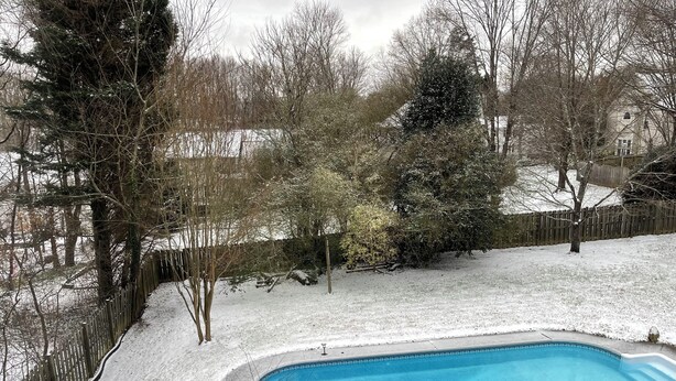 A swimming pool with a wooden deck, surrounded by snow-covered ground and trees.