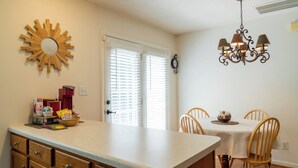 A kitchen with a large island, wooden cabinets, a chandelier, and a dining area with chairs and a table.