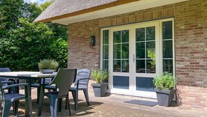 Un patio con una mesa y sillas, techo de paja y plantas en macetas.