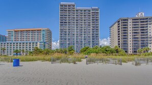 Een strandhotel met meerdere hoge gebouwen, een zandstrand en een hek dat het strand van het hotelgedeelte scheidt.