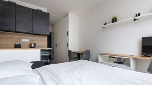 Una habitación de hotel moderna con cama, escritorio, silla, televisor y kitchenette.