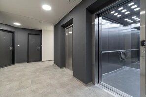 Un ascenseur moderne doté d’une porte en verre, d’une rampe métallique et d’un panneau de commande avec un bouton.