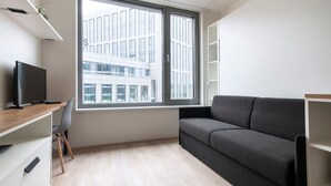 Una habitación moderna con escritorio, un sofá gris, un ventanal y vistas a un edificio.