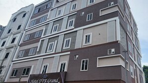 Ein mehrstöckiges Hotel mit modernem Design, das Ziegel- und Natursteinfassaden, große Fenster und eine auffällige Schilder für das Hotel D.V.R Grand zeigt.
