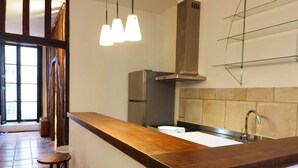 A modern kitchen with a wooden countertop, bar stools, a stainless steel refrigerator, and pendant lights.