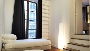 A hotel room with a bed, a window with curtains, a bedside lamp, and a staircase.