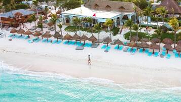 Un resort sulla spiaggia con piscina, lettini e ombrelloni di paglia.