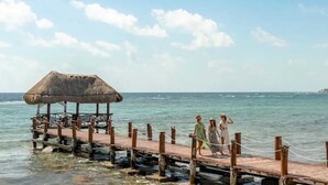 Une jetée en bois surmontée d’une structure au toit de chaume, qui mène à une mer calme.