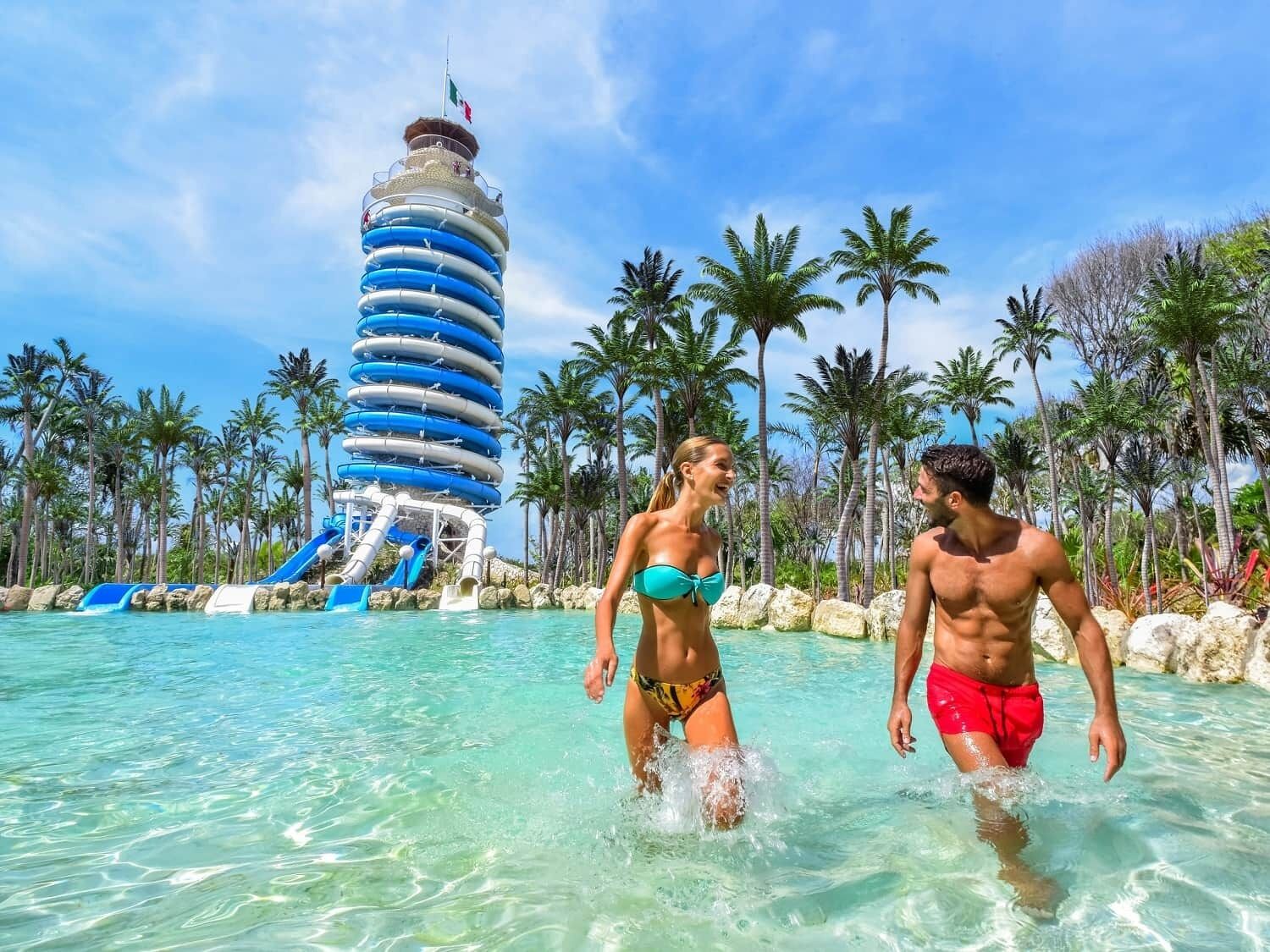 Een waterpark met een hoge, cilindervormige glijbaan en helder turquoise water.