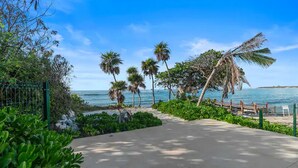 Une promenade en bord de mer bordée de palmiers, avec une clôture et une vue dégagée sur l’océan.