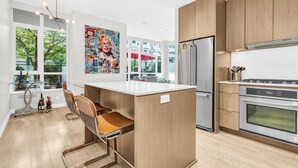 Une cuisine moderne dotée d’un îlot central, d’appareils électroménagers en acier inoxydable et de grandes fenêtres offrant une vue sur l’extérieur.