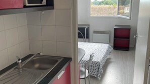 Cocina compacta con microondas, fregadero y estufa. Se observa un comedor con mesa y sillas a través de un acceso abierto.