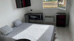 Un dormitorio con cama, escritorio, silla, televisor y ventana con vista al campo.