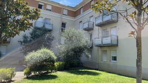 Un patio con un edificio que presenta varios balcones, rodeado de vegetación y un cielo despejado.