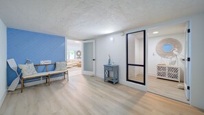 A spacious room with a wooden floor, a blue accent wall, a wooden bench with cushions, a small side table, and a large mirror on a white cabinet. - Spacious 4-bedroom Key Largo Villa steps from the pool, pickleball, & marina.  (Key Largo)