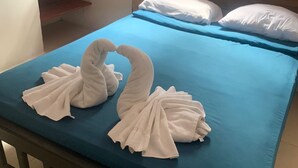 A bed with a blue mattress and white pillows, a wooden headboard, and a wooden bench with a white towel folded into a swan shape. - Hotel La Ceiba Panamá  (San José del General)