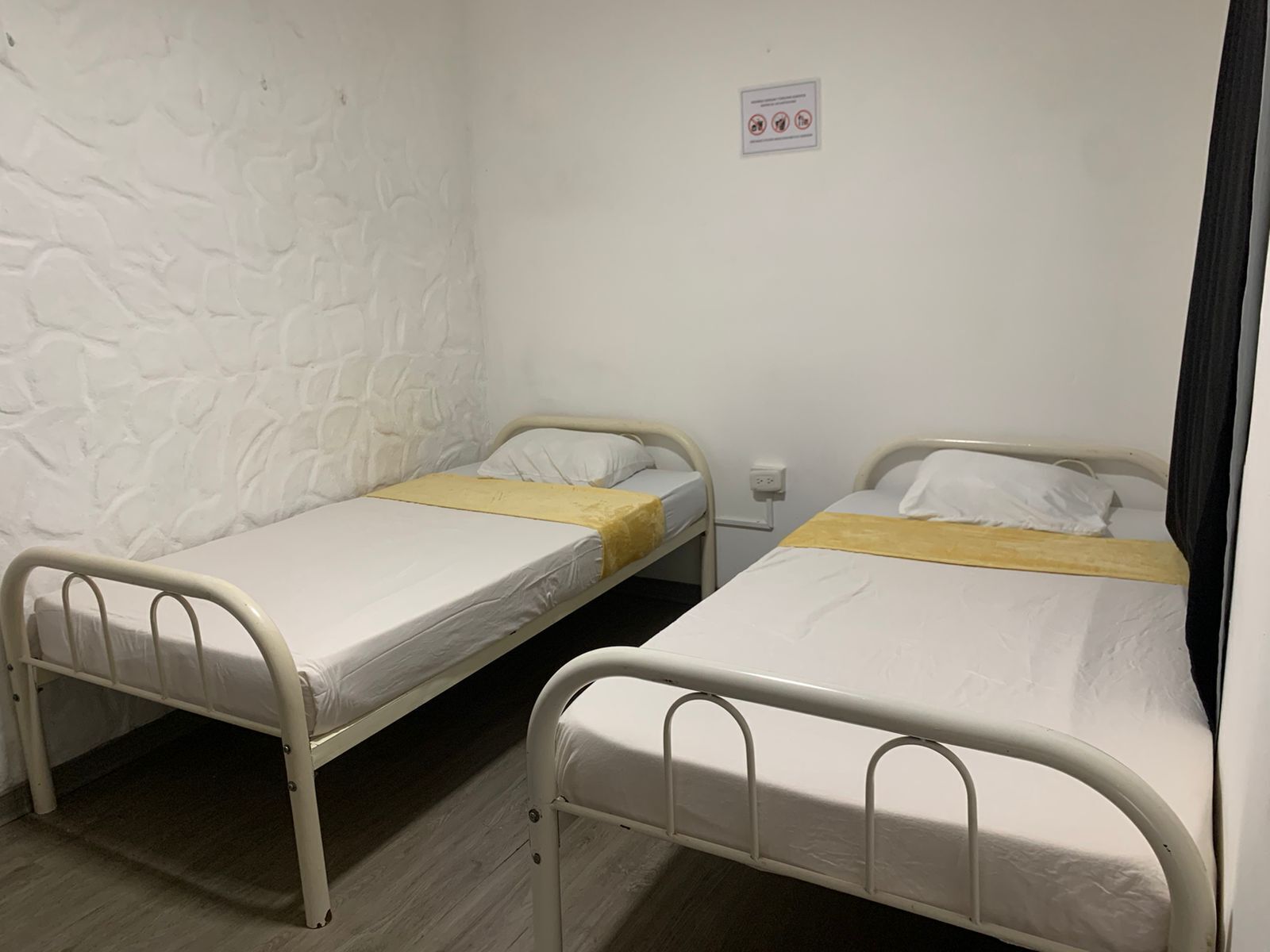 Two single beds with white bedding and yellow headboards in a room with a textured white wall and a small sign on the wall.