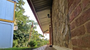 A covered walkway with stone flooring, a brick wall, and a metal roof. - Hotel La Ceiba Panamá  (San José del General)