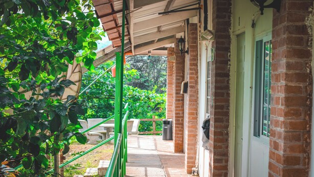 A covered outdoor area with a brick wall, a green railing, and a pathway leading to a door. - Hotel La Ceiba Panamá  (San José del General)