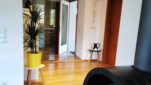 Una sala moderna con piso de madera, una chimenea negra grande, una puerta de cristal que da a otra habitación y una planta amarilla en maceta.