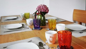 Una mesa de comedor dispuesta con platos, cubiertos, vasos y un jarrón con flores.