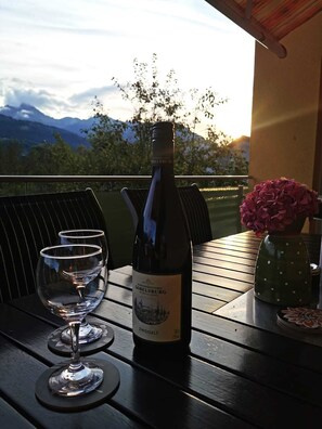 Eine Weinflasche auf einem Tisch mit zwei Gläsern, einer Blumenvase und einem weiten Blick auf Berge im Hintergrund.