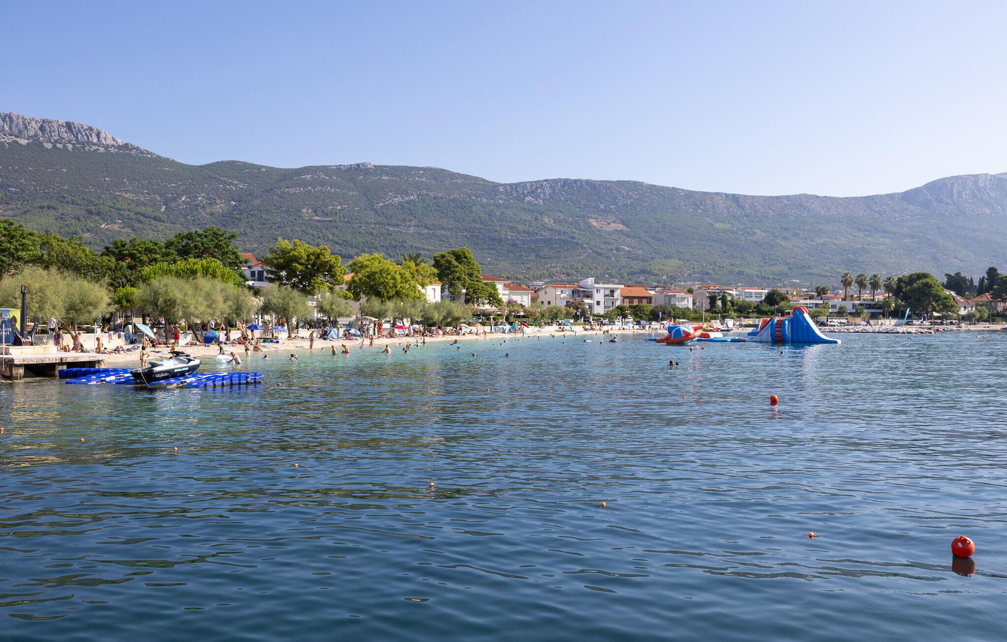 A beach with clear waters, a few boats, and a water park.
